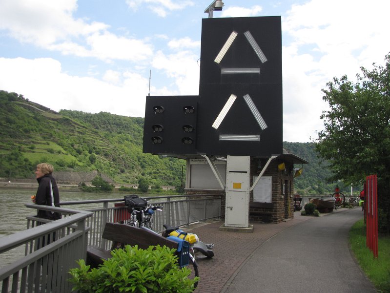 waarschuwingslicht loreley.jpg - Rond de Loreley is de Rijn over een afstand van 5 km zeer smal en maakt vele bochten. Schepen kunnen elkaar hier slecht zien en radioverkeer is door de hoge bergen ook lastig. Daarvandaan dat hier voor schepen die stroomopwaarts gaan signalen neergezet zijn. Dit deel van de Rijn is verdeeld in 4 sectoren. Het signaal op de foto geeft aan dat er minstens 1 schip tot 110 meter lang in sector 4 zit en minstens 1 schip tot 110 meter in sector 3 (verkeer dat stroomafwaarts gaat). Branden de lampen in de vorm van een dak, dan is er minstens 1 schip langer dan 110 meter in de sector die stroomafwaarts gaat. Brand de horizontale balk dan zit er geen verkeer dat stroomafwaarts gaat in die sector.